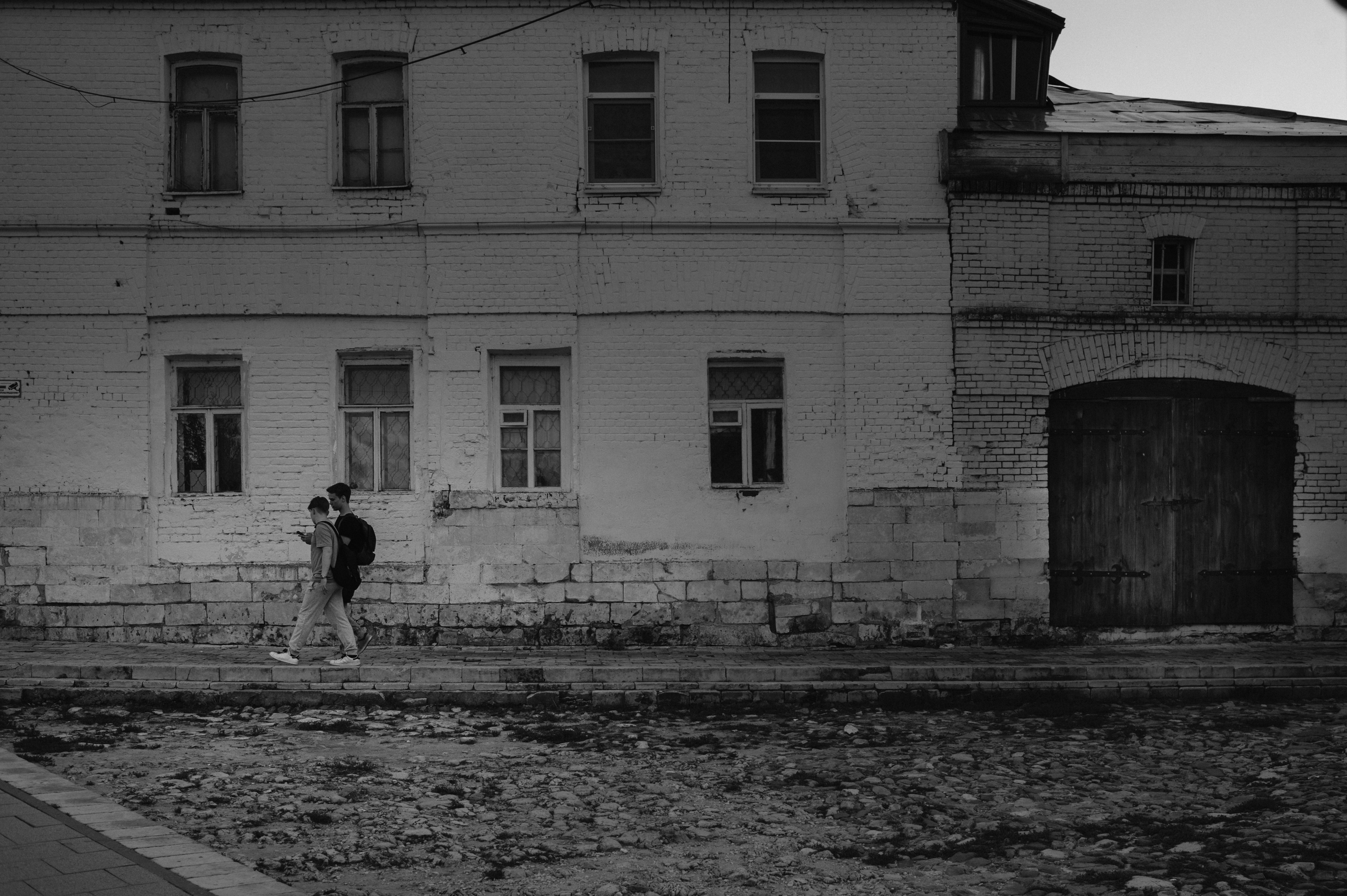 Two young men walk along the facade of an old house.